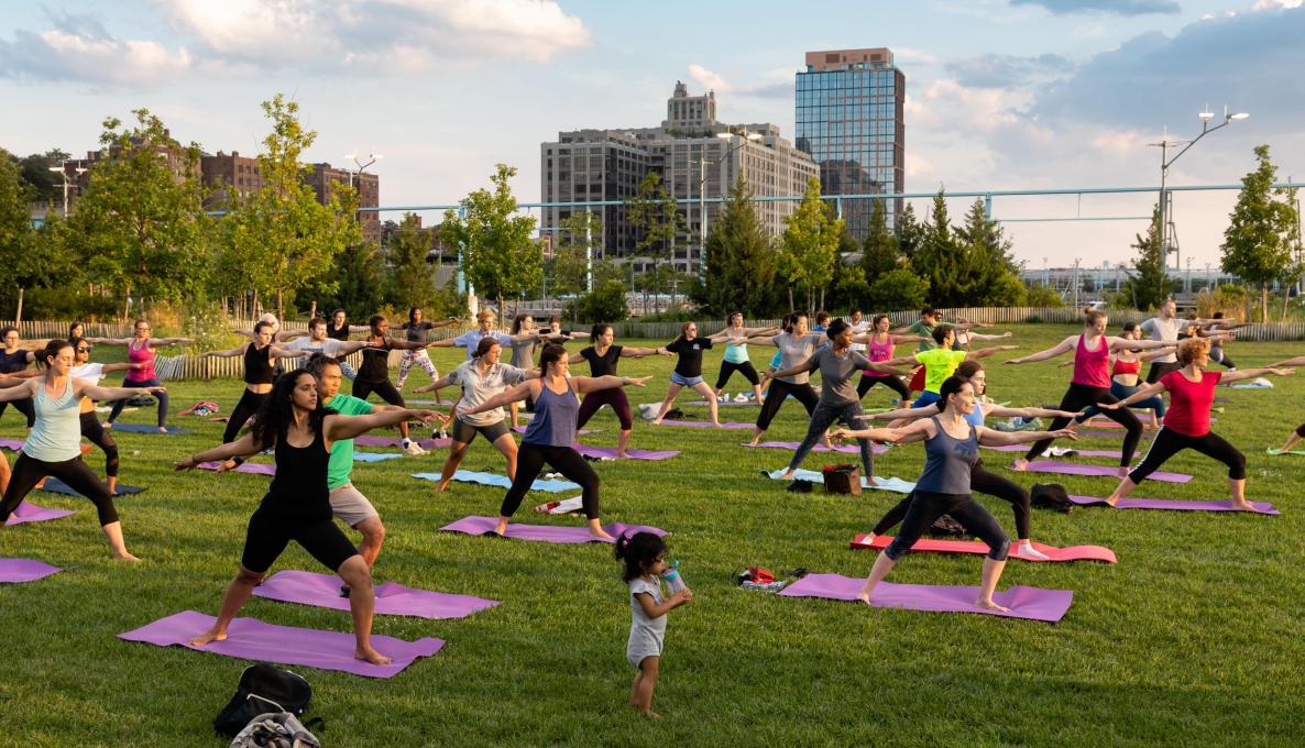 People on yoga mats doing warrior two pose at sunset.