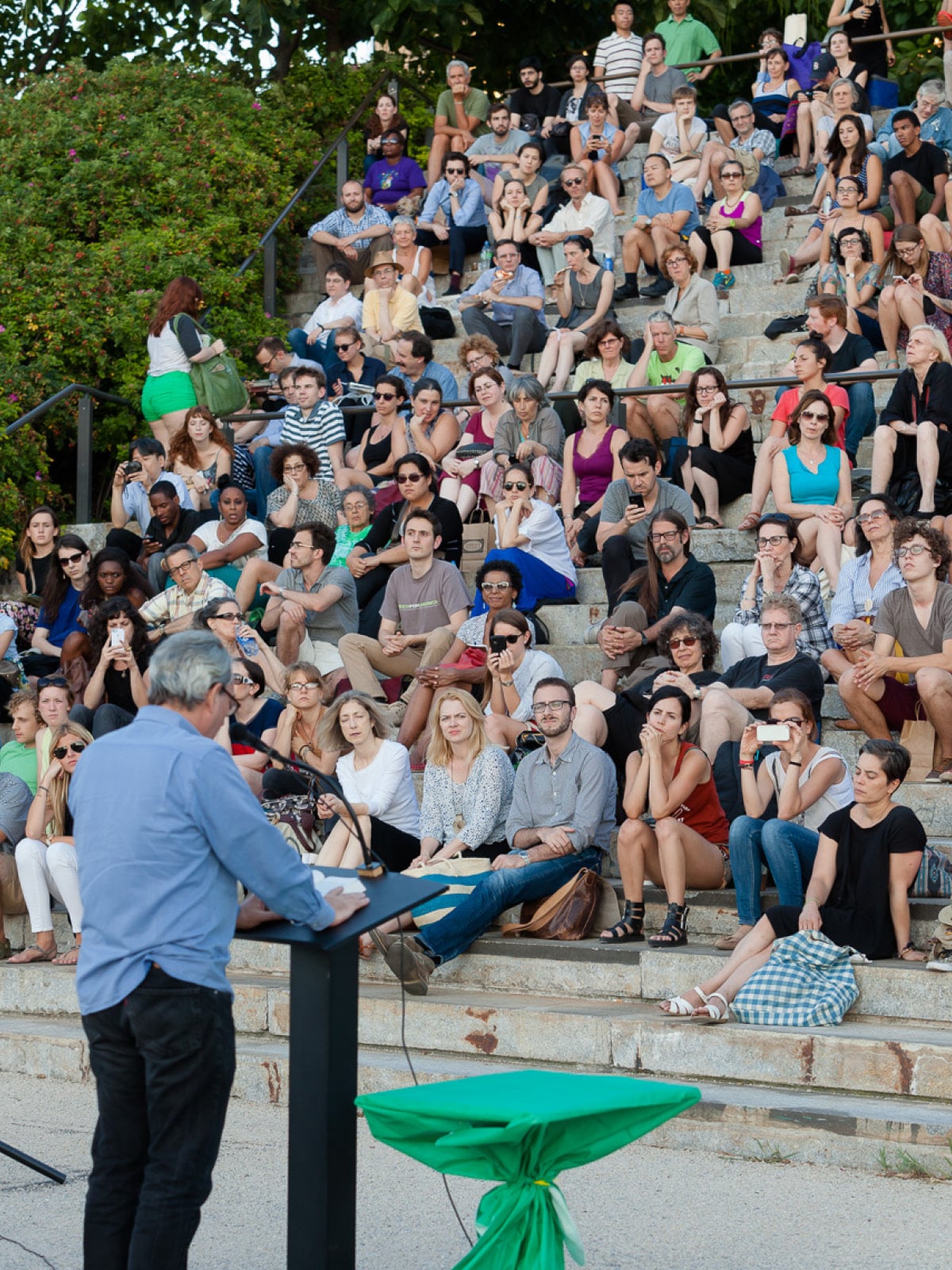 Man with his back turned reading to a crowd.