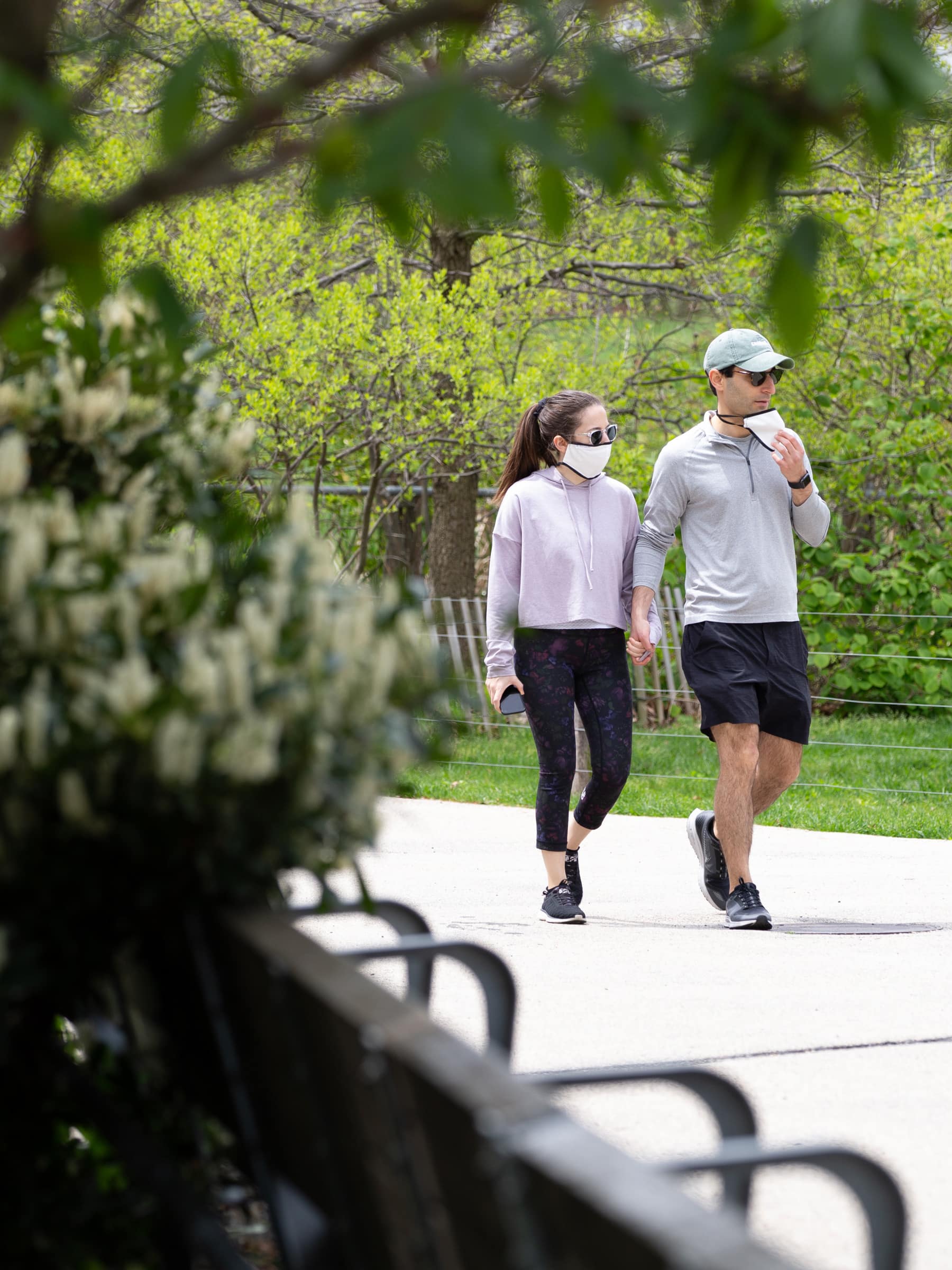 Couple with masks walking by benches on the Greenway on a sunny day.