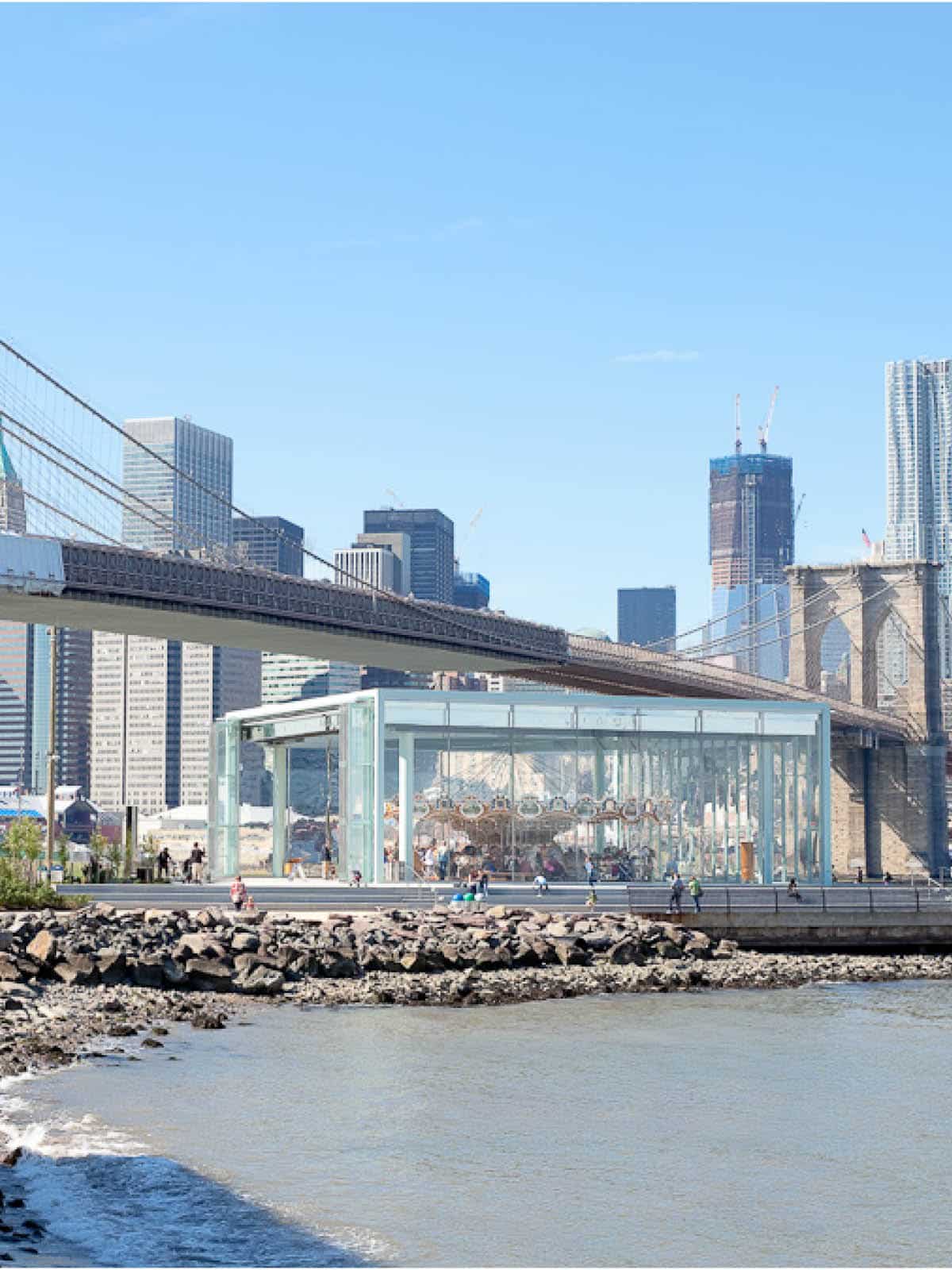 View of Jane's Carousel at Empire Fulton Ferry on a sunny day. The Brooklyn Bridge is seen in the background.