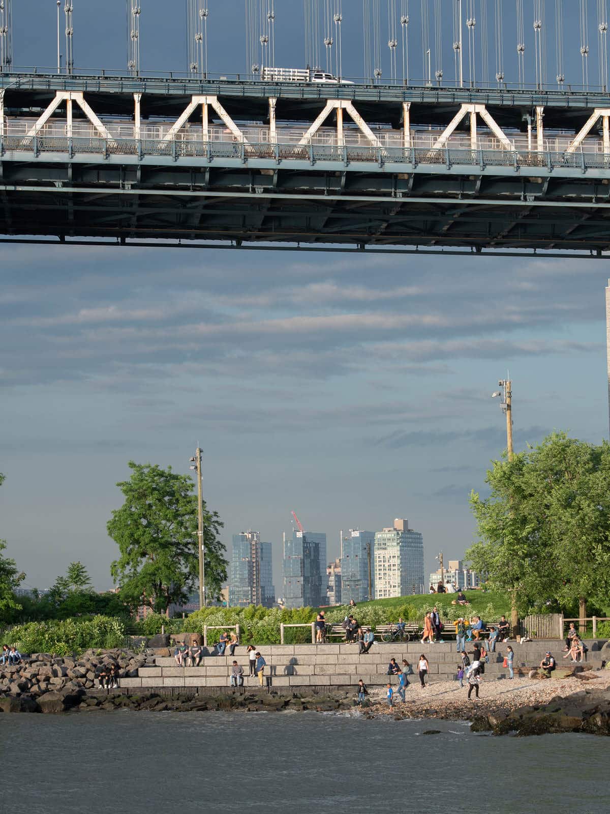 Groups of people sitting on the step by Pebble Beach under the Manhattan Bridge at sunset.