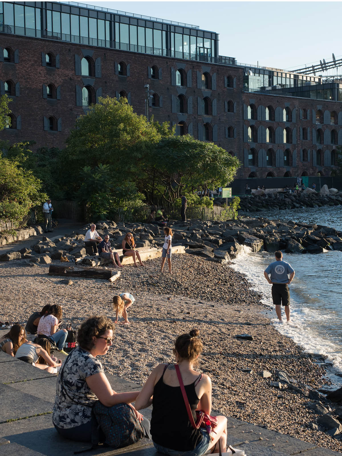 People sitting on the steps beside Pebble Beach at sunset with buildings in the background.