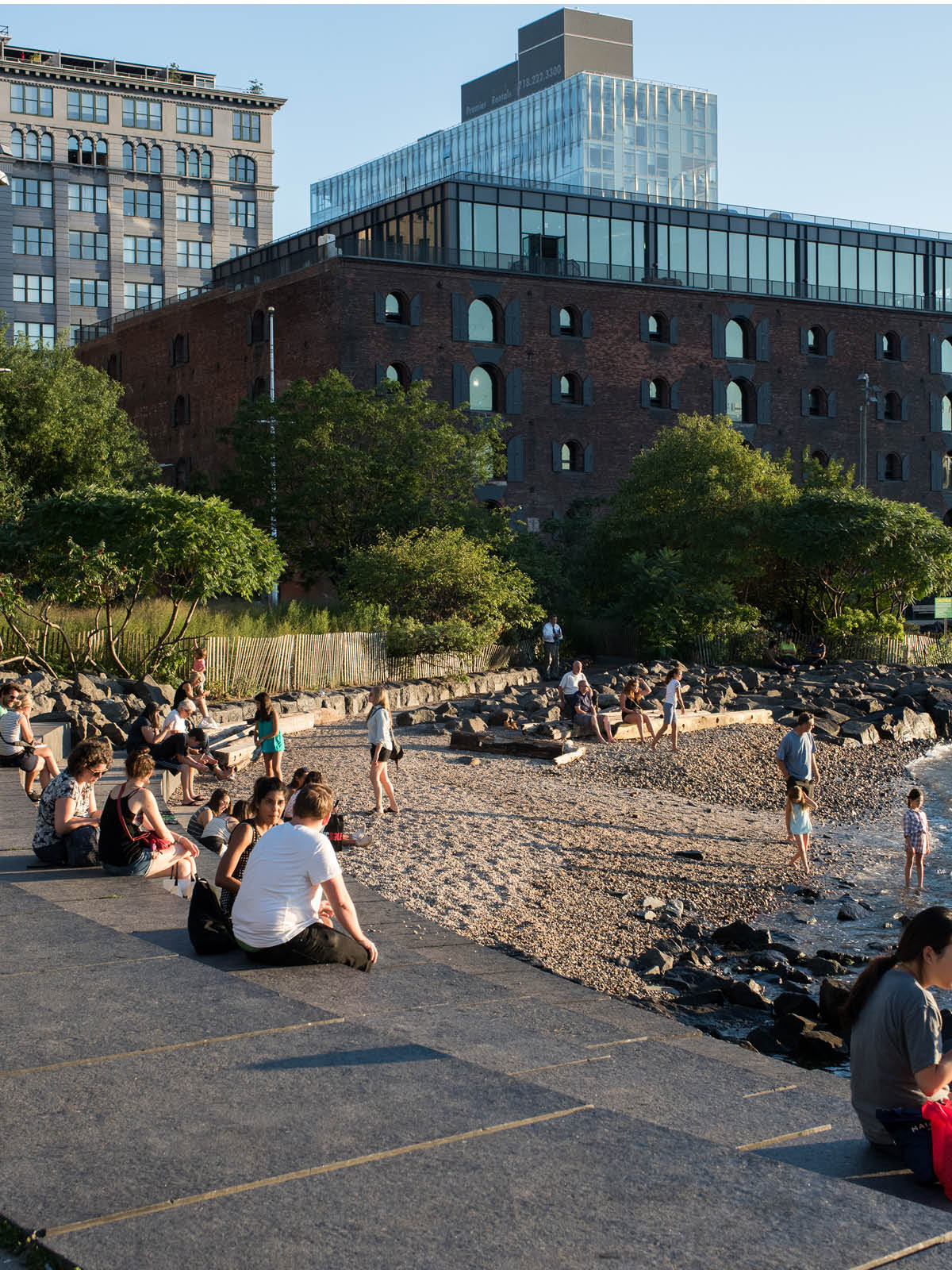 People sitting on the steps beside Pebble Beach at sunset with buildings in the background.