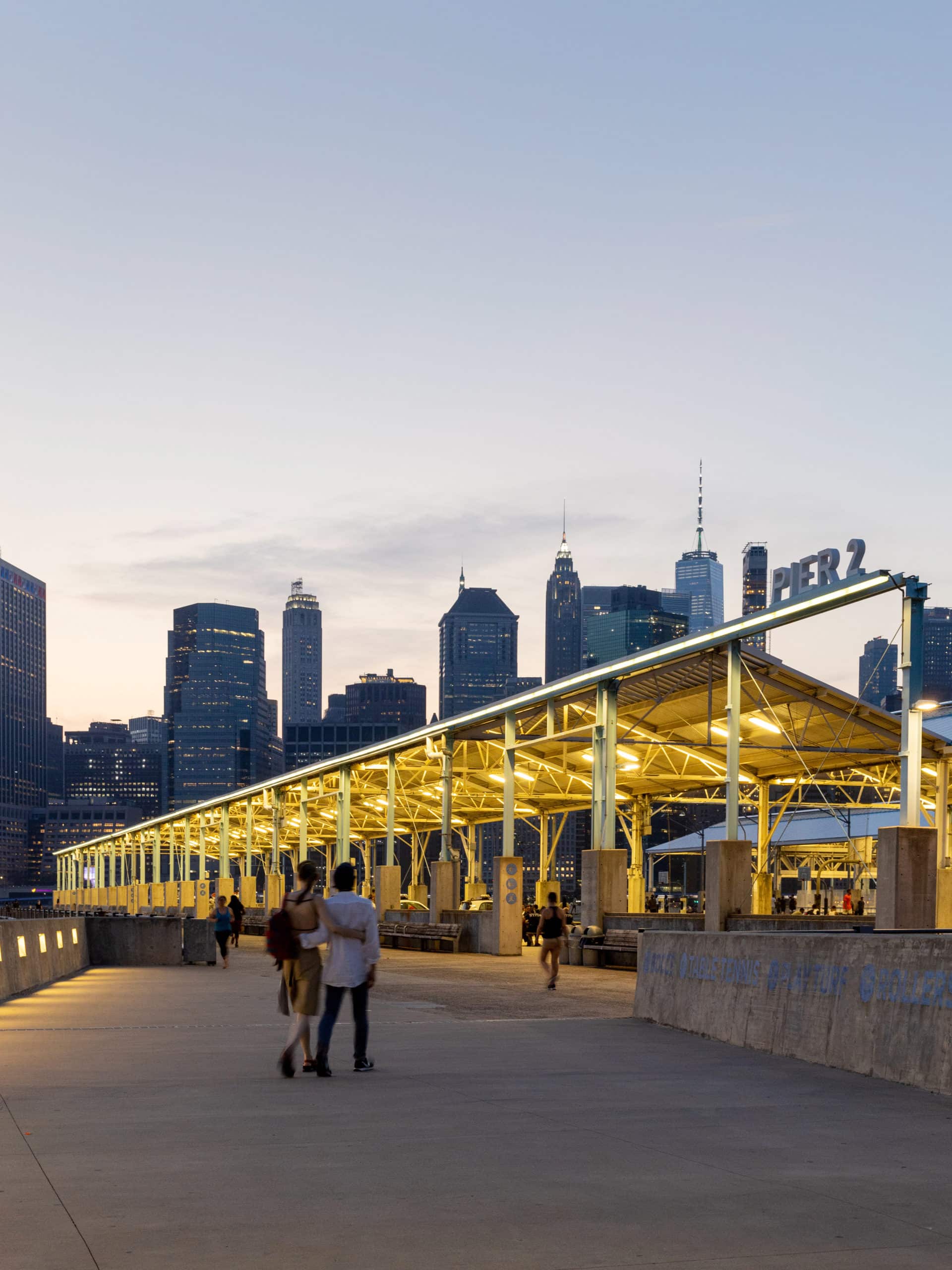 Couple walking down Pier 2 Promenade at night, illuminated by the Pier 2 roof lights.