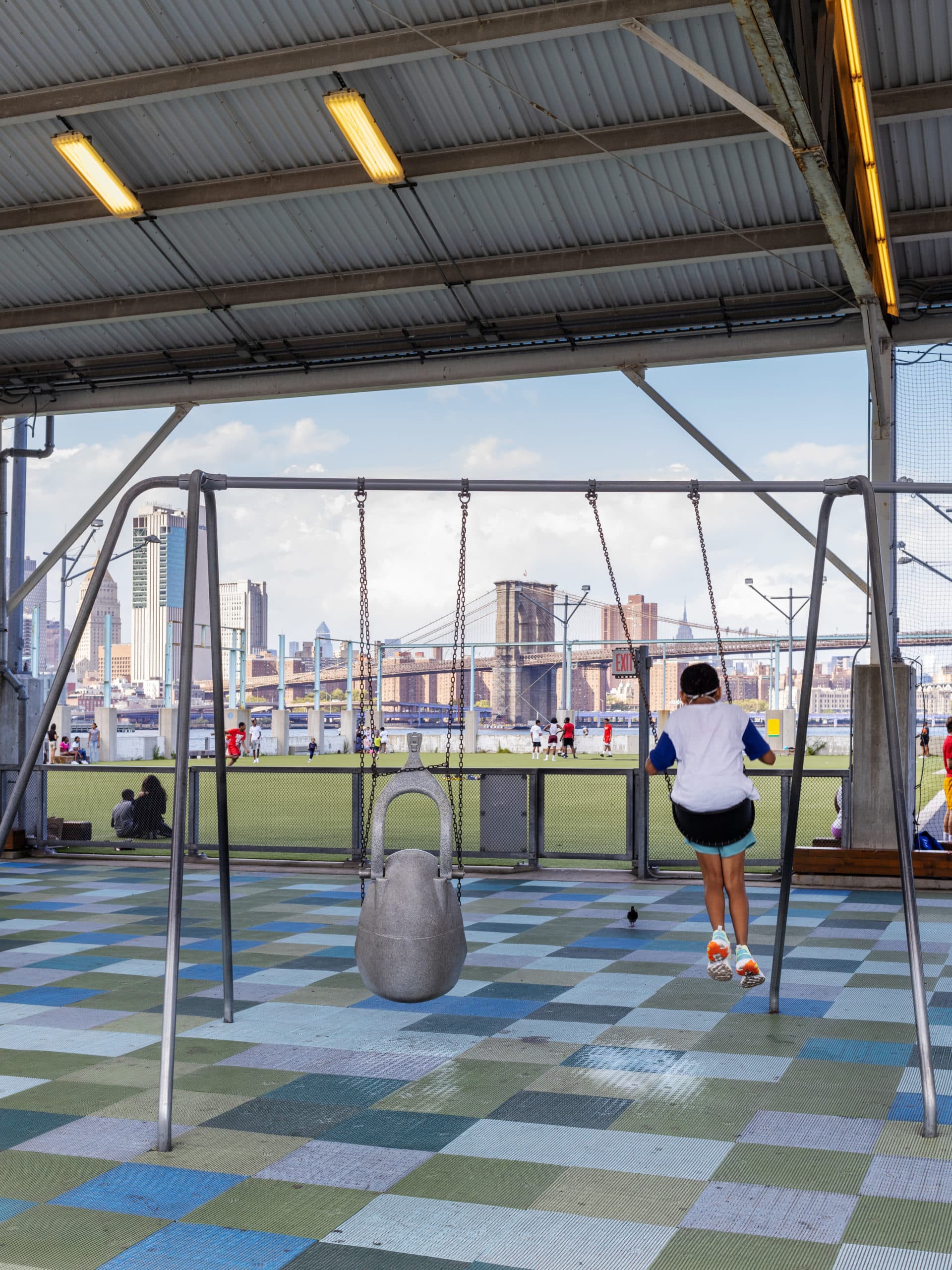 Boy swinging on the swings at Pier 2 with the Brooklyn Bridge in the distance.