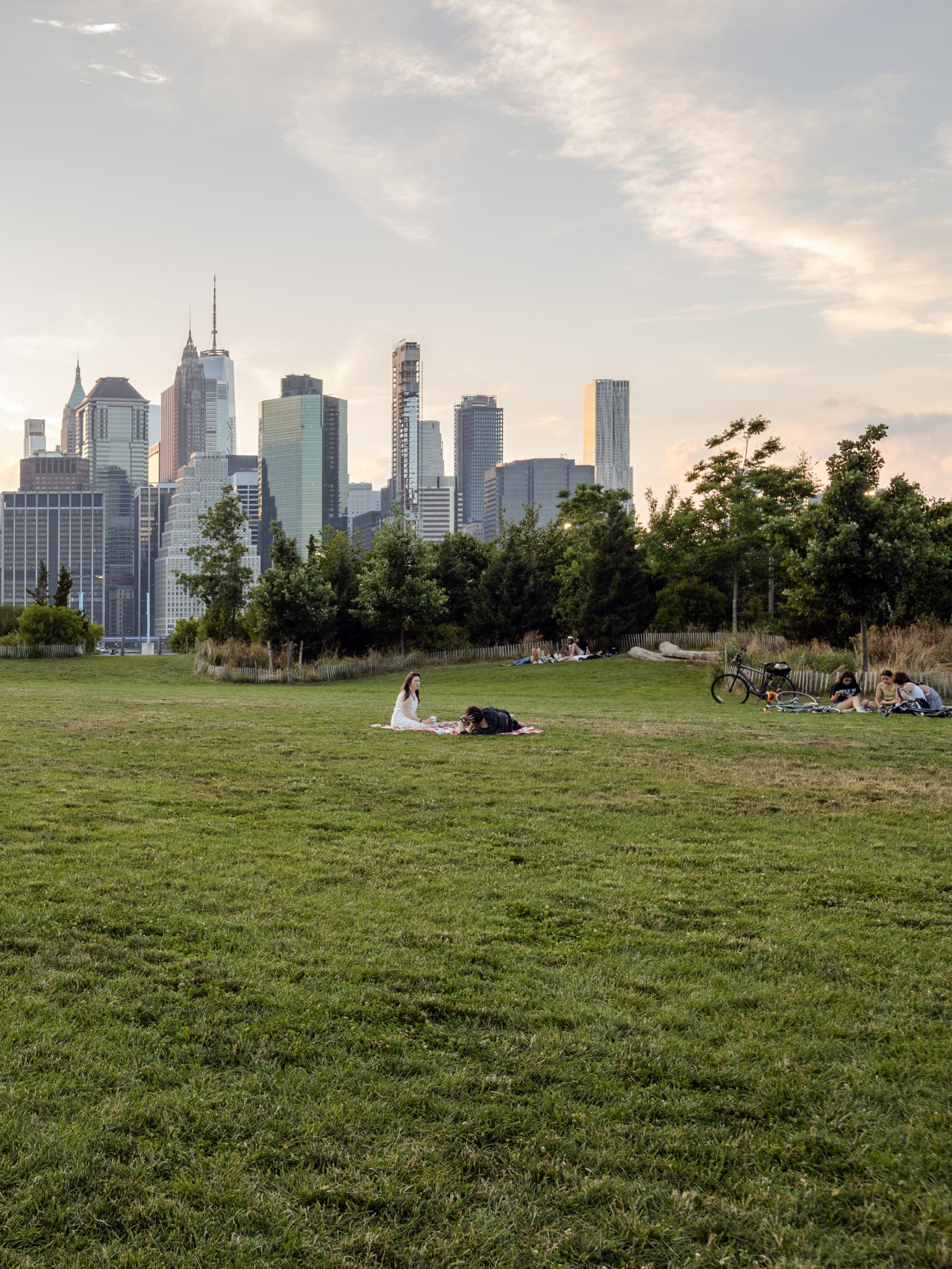 People sitting on Pier 3 Lawn at sunset with view of lower Manhattan.