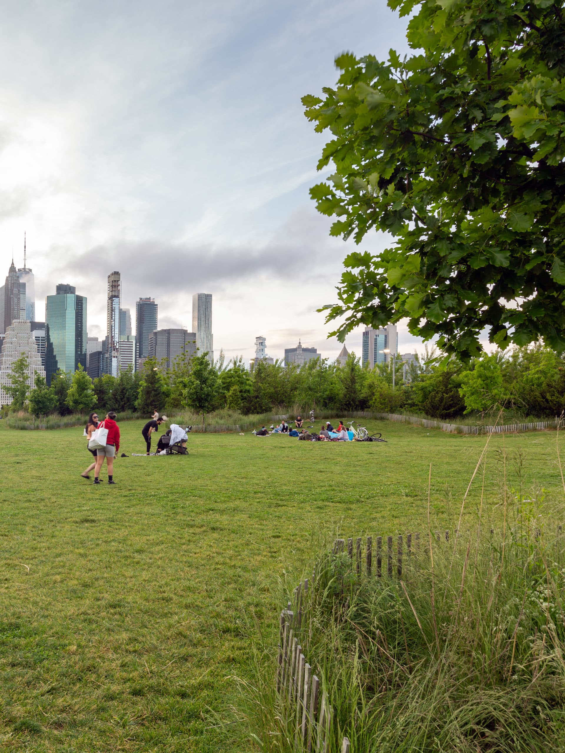 People sitting on Pier 3 Lawn at sunset with view of lower Manhattan.