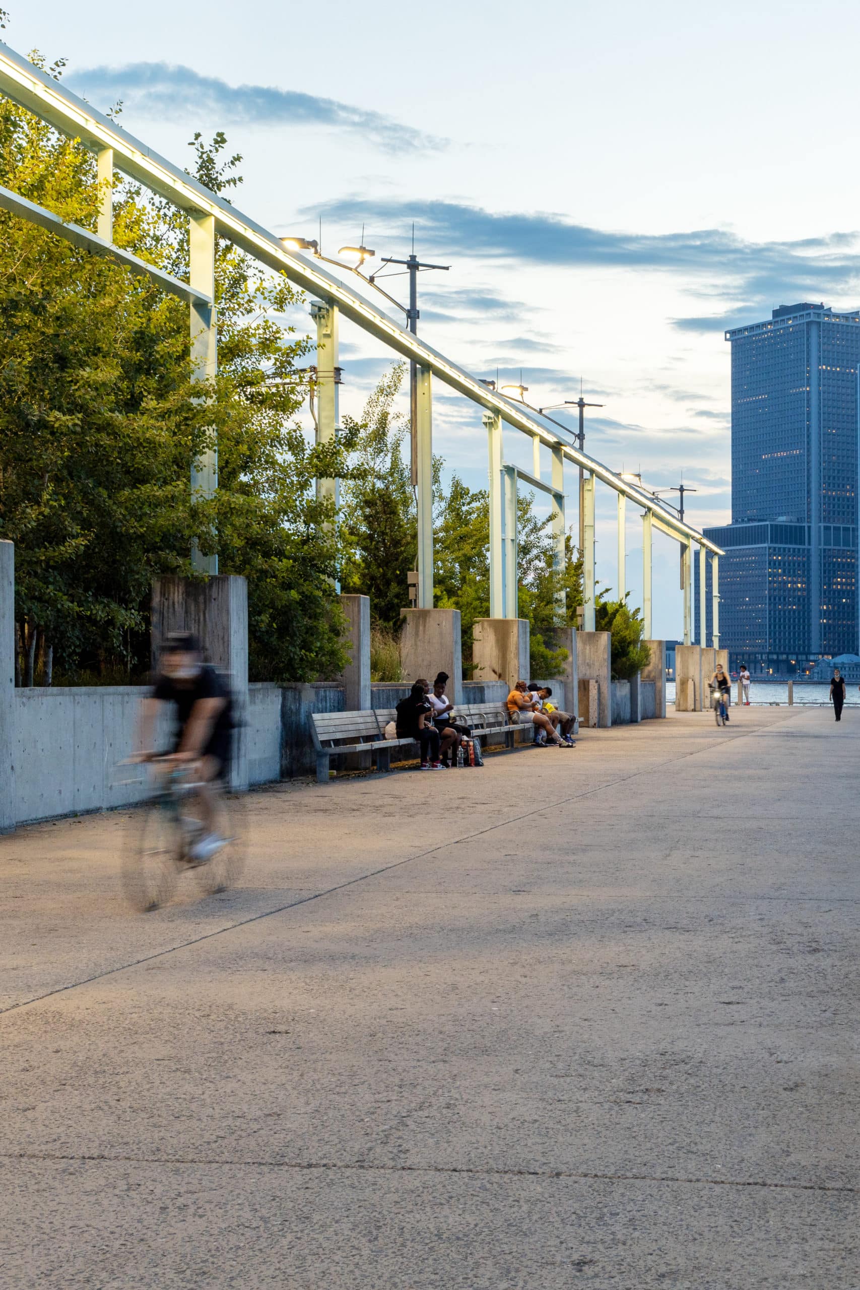 People biking and sitting on benches at the Pier 3 Promenade at dusk.