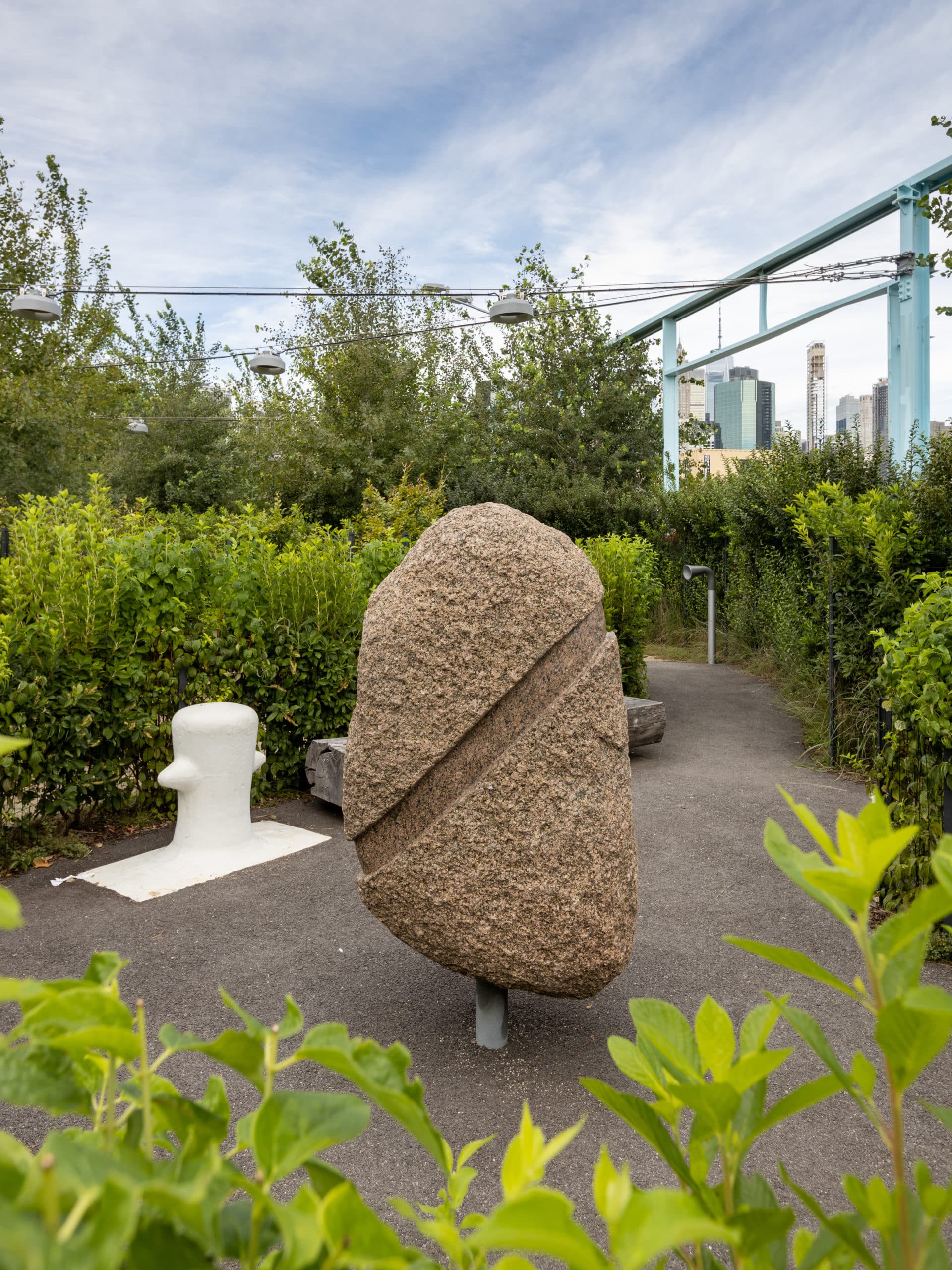 Rock sculpture on a path surrounded by bushes and trees on a cloudy day.