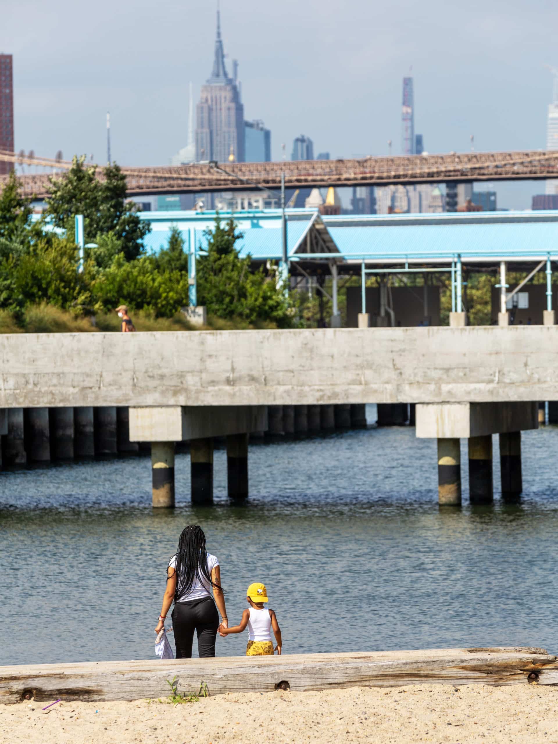 Woman and child holding hands on the Pier 4 Beach looking at the bridge to Pier 3 on a sunny day.