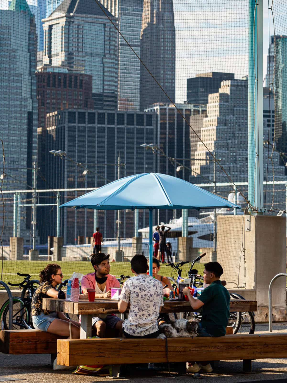 People sitting around a picnic table under a umbrella on a sunny day.