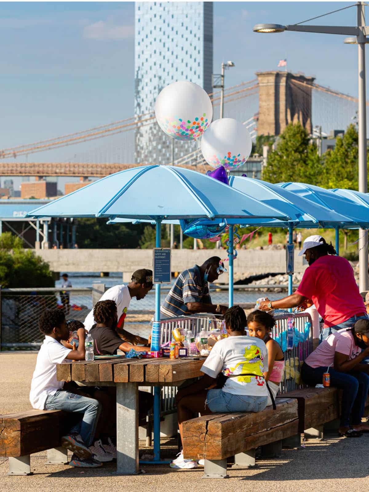 People sitting around a picnic table under a umbrella on a sunny day.