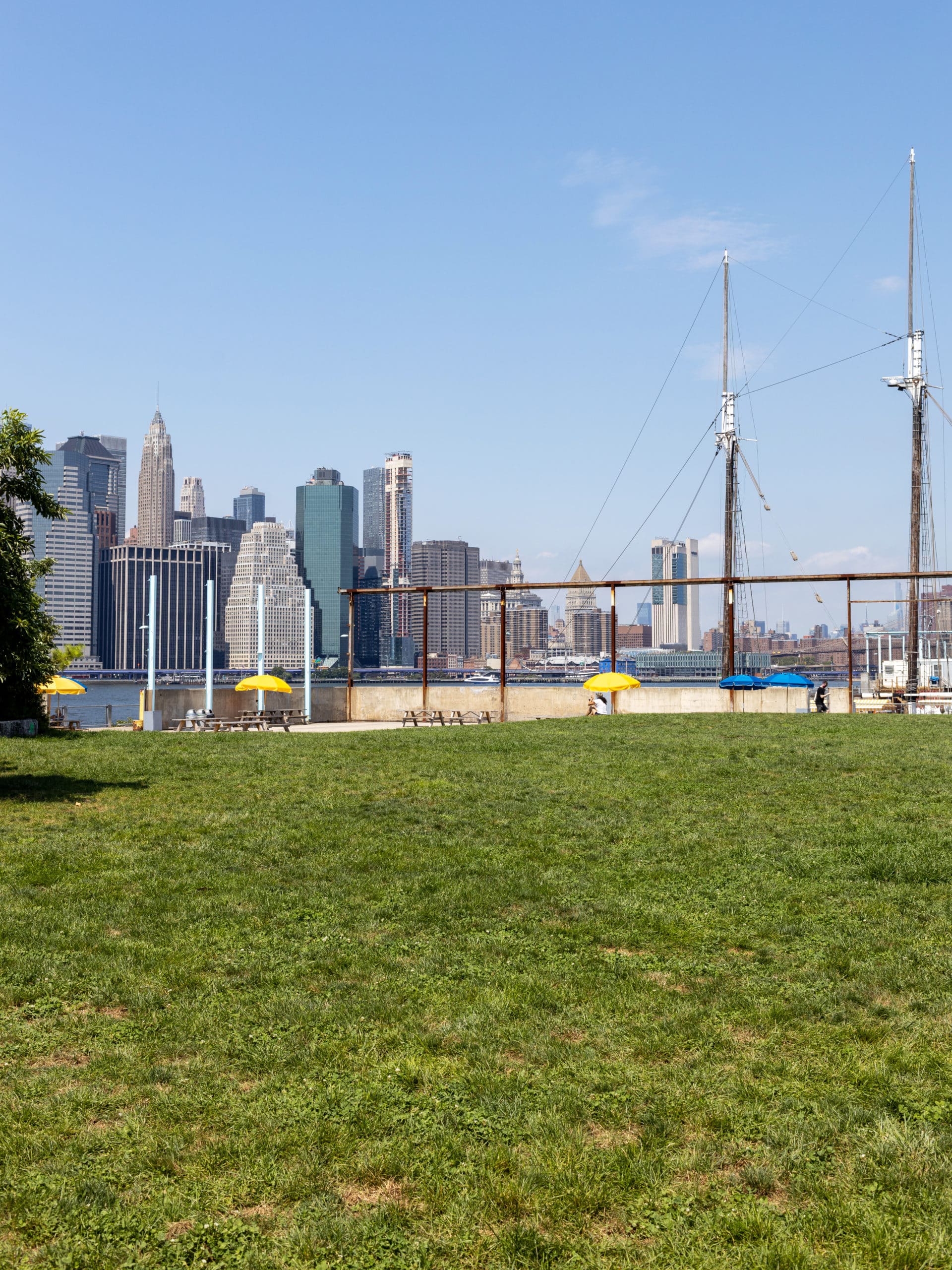 Lawn with picnic benches and Pilot restaurant boat seen in the background on a sunny day.