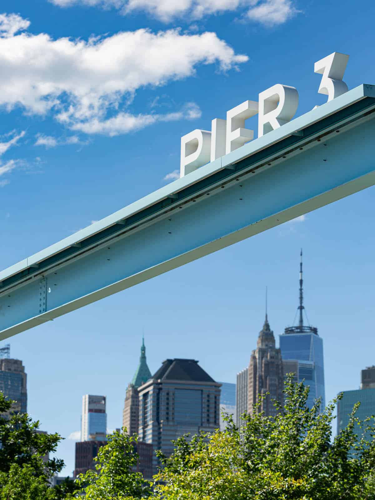 Sign over Pier 3 Entrance on a sunny day with a view of lower Manhattan.