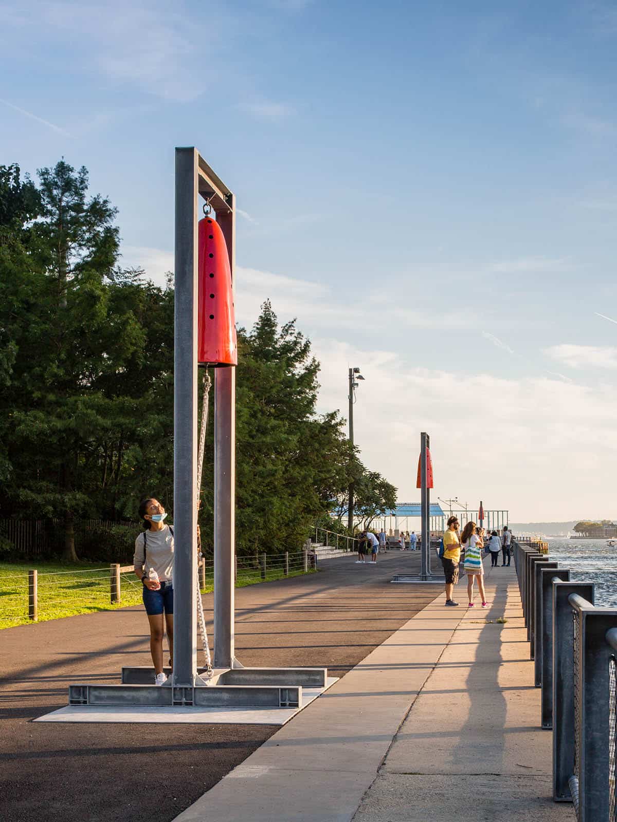 People on the Pier 1 Promenade with a view of several bells from Devina Semo's Reverberation at sunset.