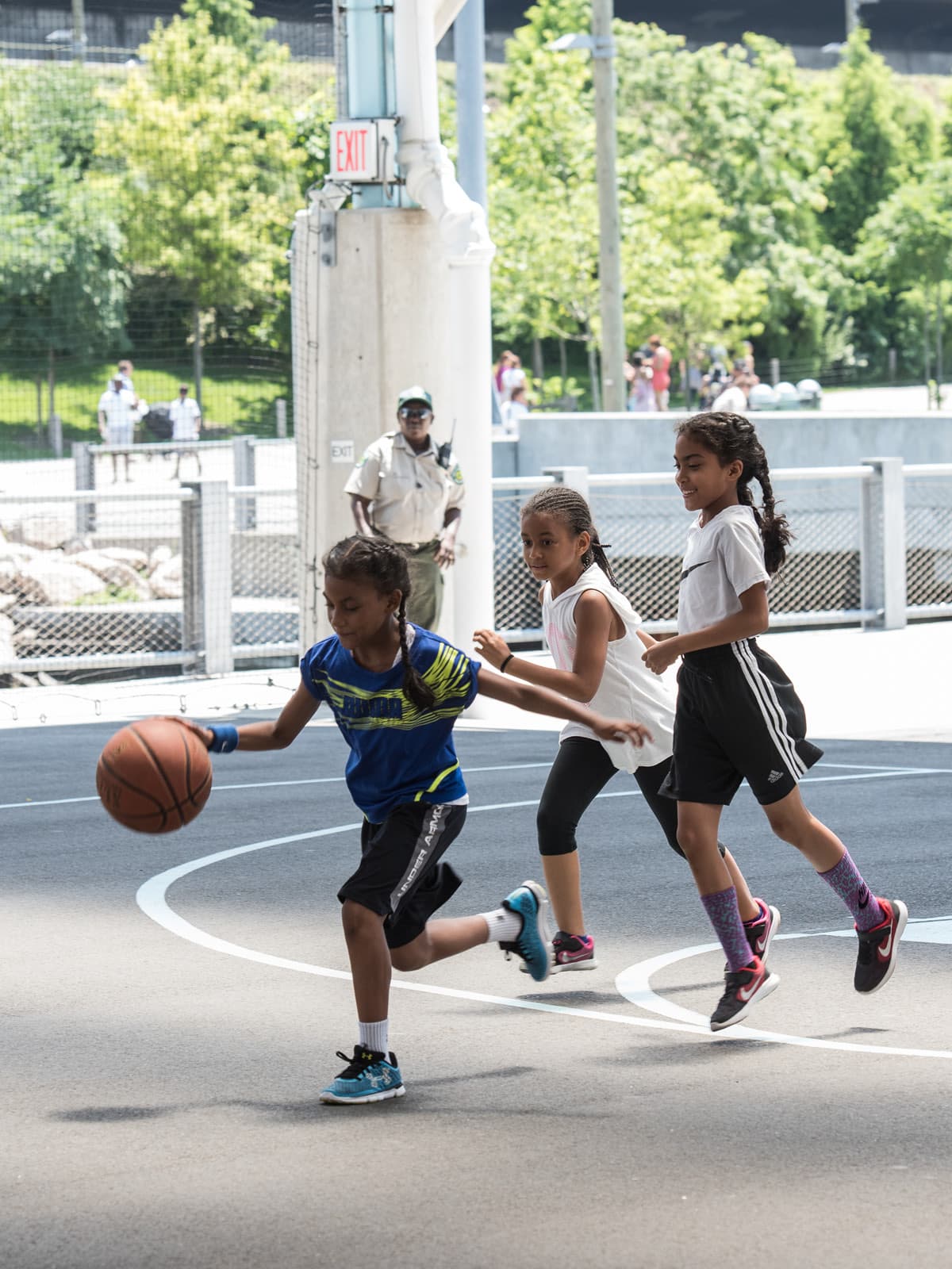 Girl running with basketball pursued by two other girls on a sunny day.