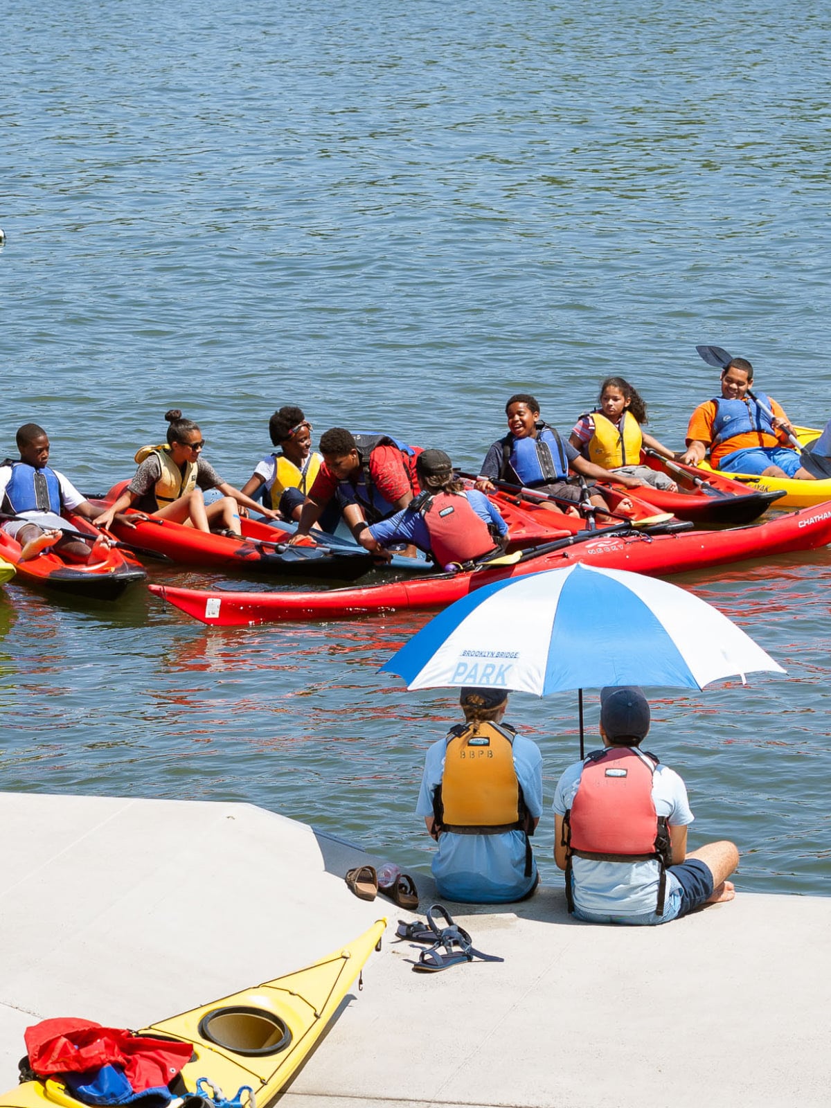 Group of teenagers in kayaks with instructors on the dock on a sunny day.