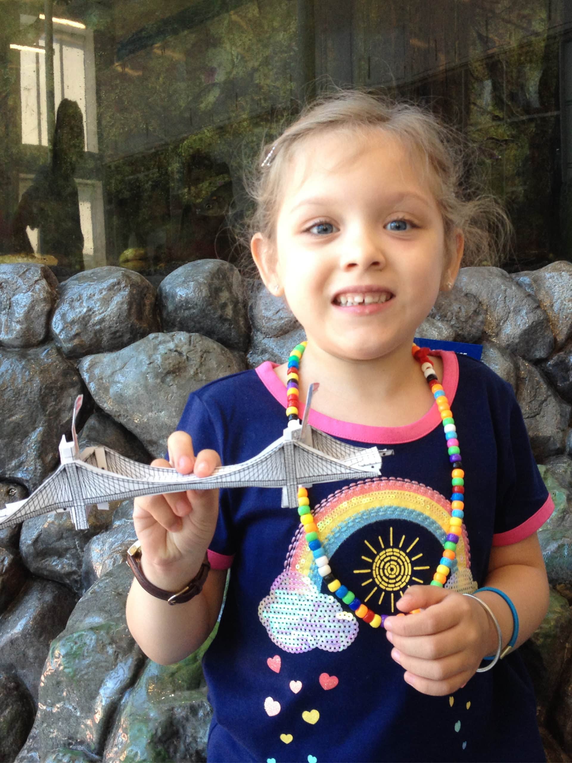 Girl holding small paper model of Brooklyn Bridge.