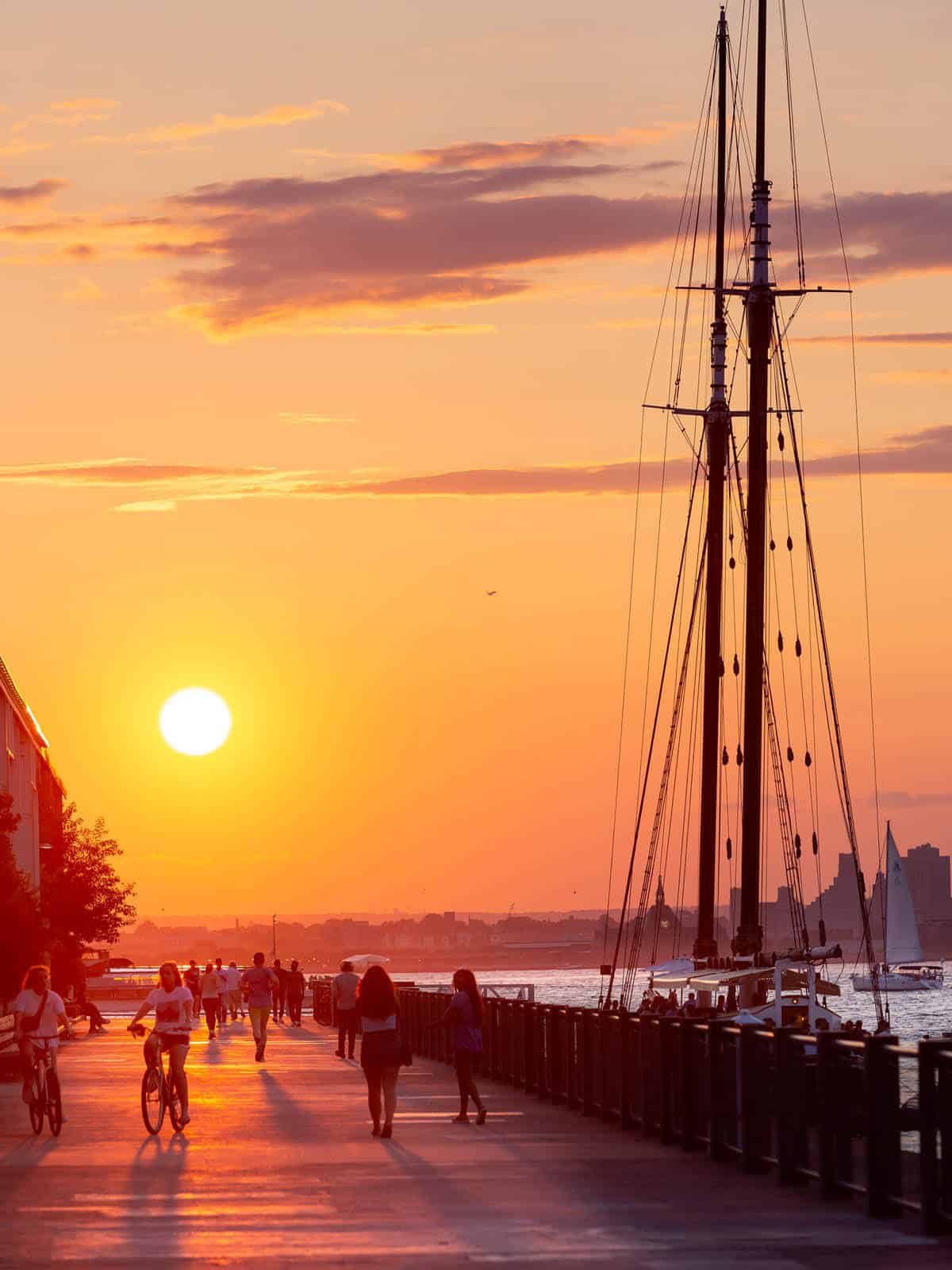 People walking on promenade at sunset with restaurant boat Pilot in the water.