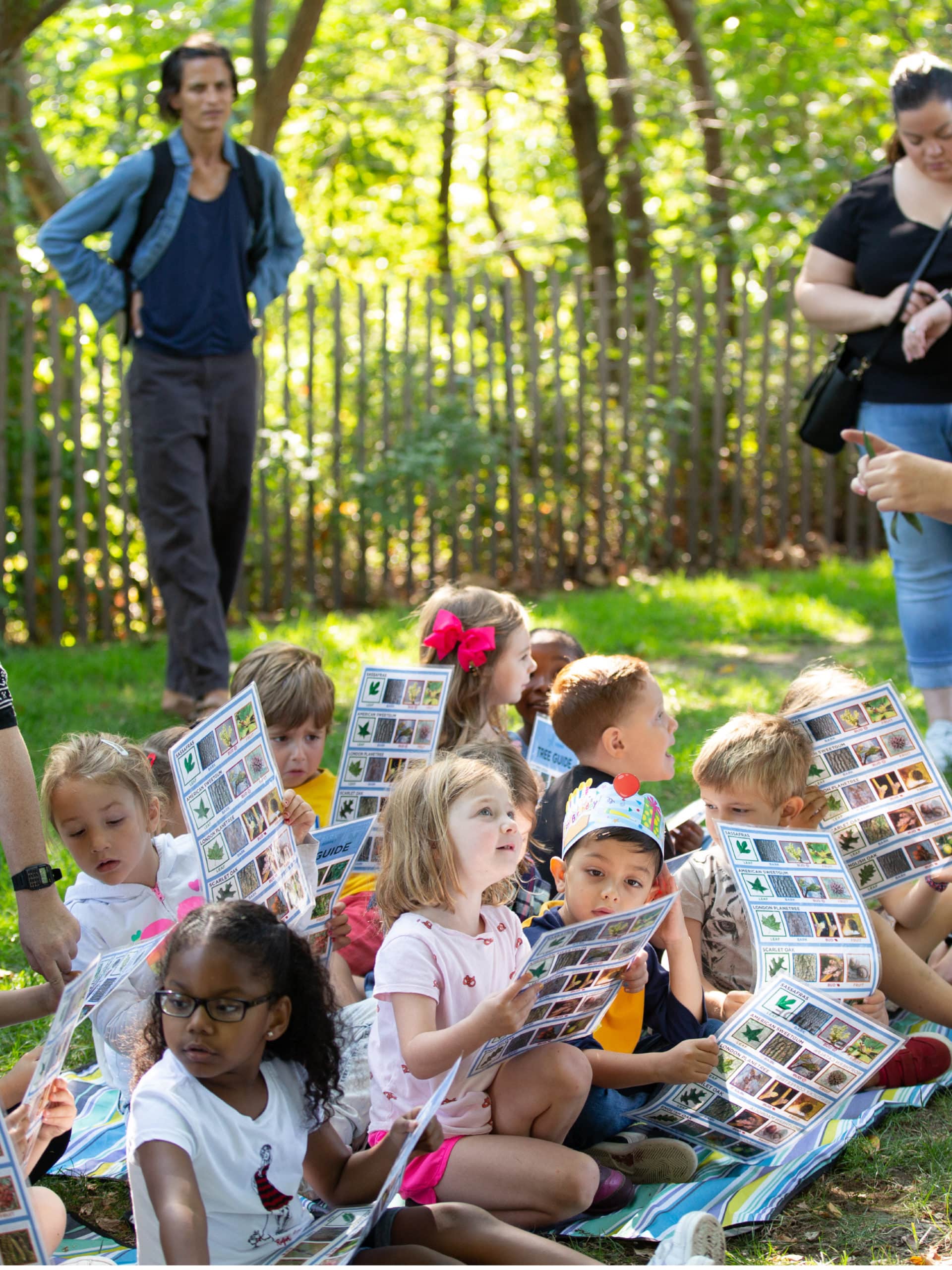 Group of schoolchildren sitting on the grass holding tree guides.