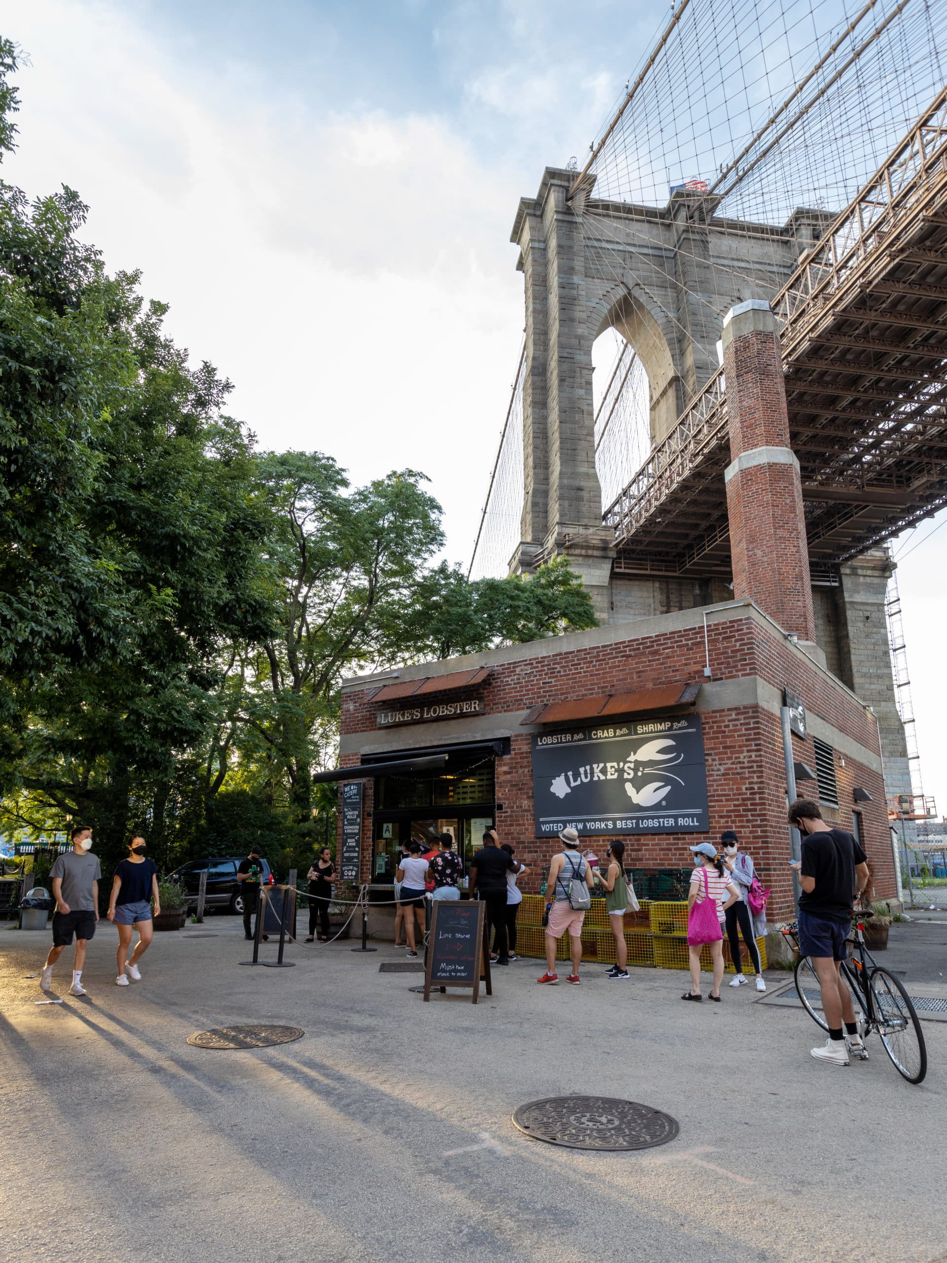 People in line for Luke's Lobster in historic Smokestack Building with Brooklyn Bridge overhead.