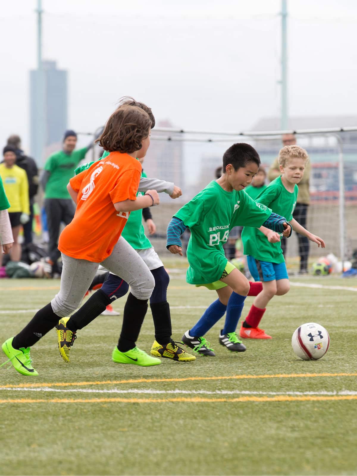 Children running after a soccer ball on a cloudy day.